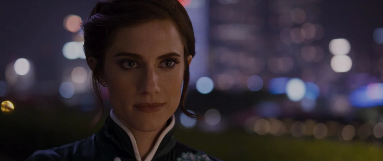 The Perfection (2018) movie still: closeup — A woman stands on a darkened rooftop overlooking an out-of-focus city night skyline. She remains still…