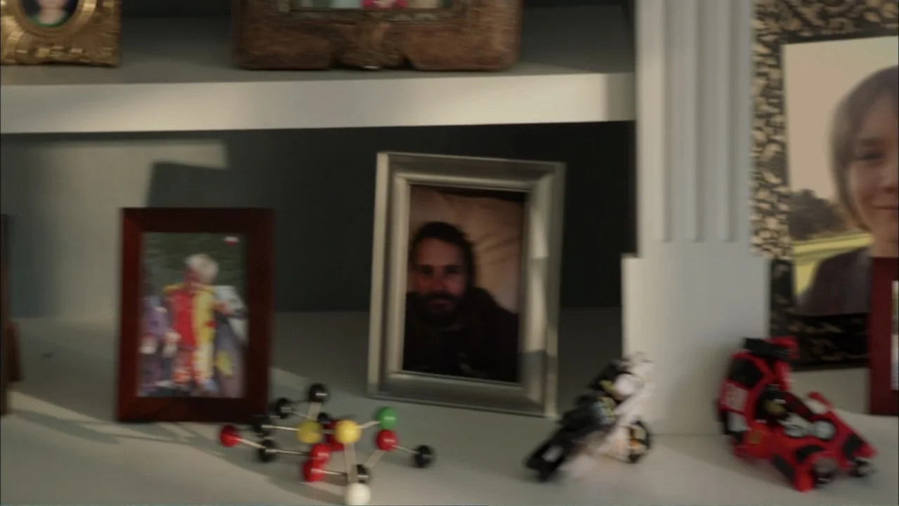Dark Skies (2013) movie still: closeup — A white mantelpiece is cluttered with framed family photographs and small plastic toys. The objects are…