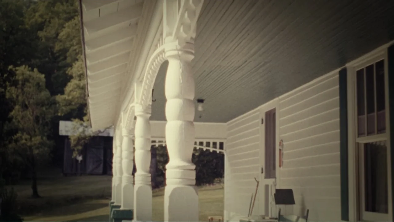 The Winding Stream (2014) movie still: wide — A rural wooden house porch with white columns and green ceiling trim stretches horizontally. The…