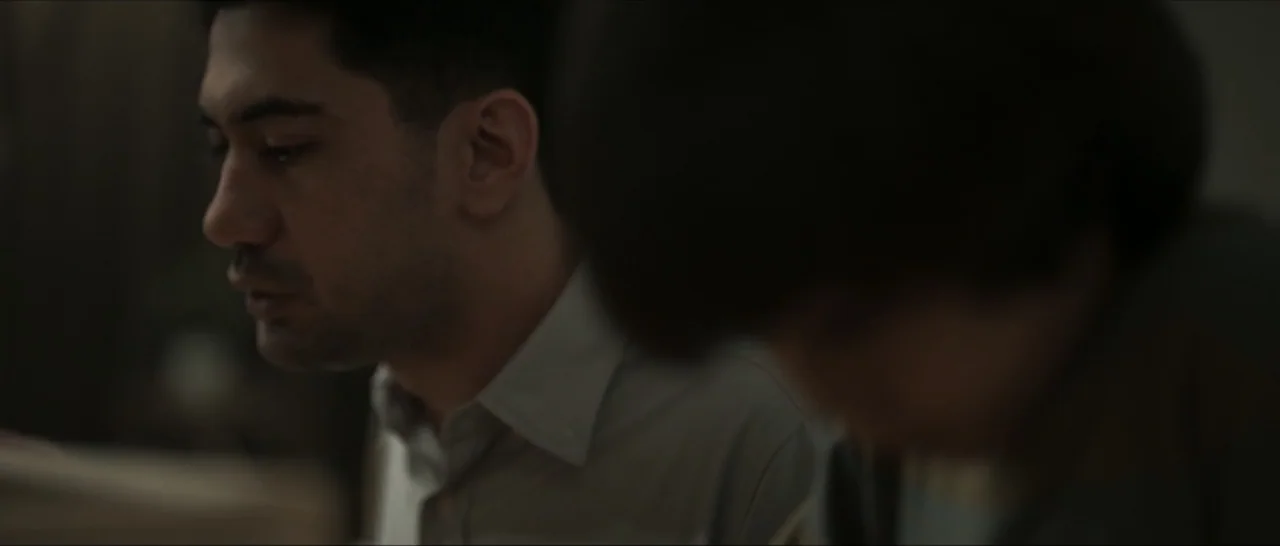 Innocent Vengeance (2023) movie still: closeup — A dimly lit room with two individuals positioned near each other. One man sits in profile while the…