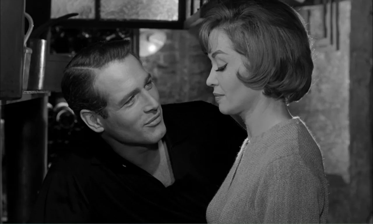 Paris Blues (1961) movie still: medium — A dimly lit indoor space with textured wall surfaces and kitchen elements present. A man stands close to a…