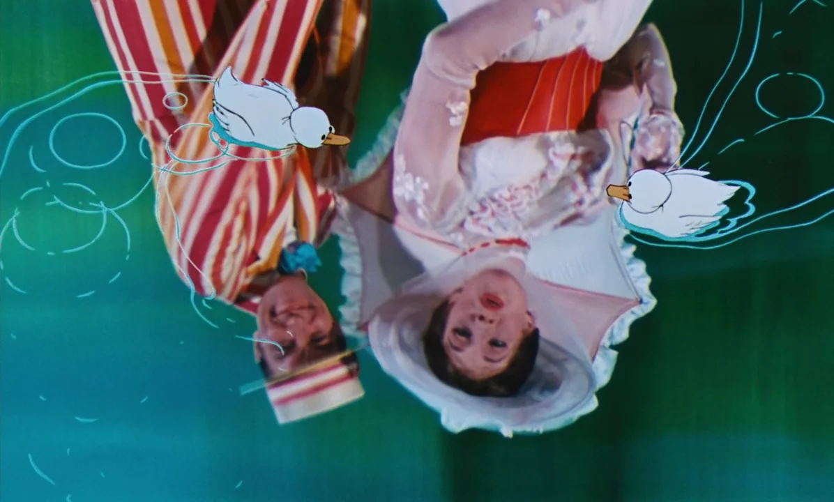 Mary Poppins (1964) movie still: medium — A man and a woman lie in a field surrounded by animated ducks. The scene incorporates hand-drawn animated…