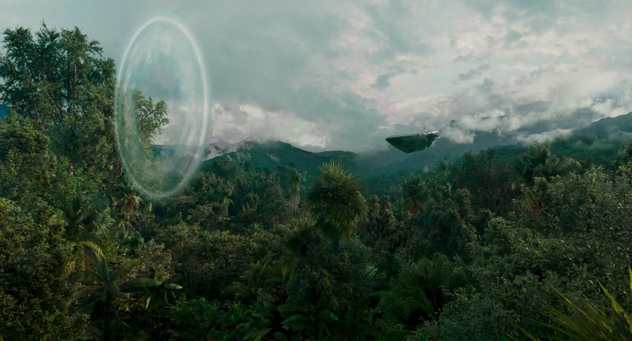 Memoria (2021) movie still: establishing — A dense, overgrown jungle landscape sits beneath a cloudy, overcast sky during the day. A smooth metallic…