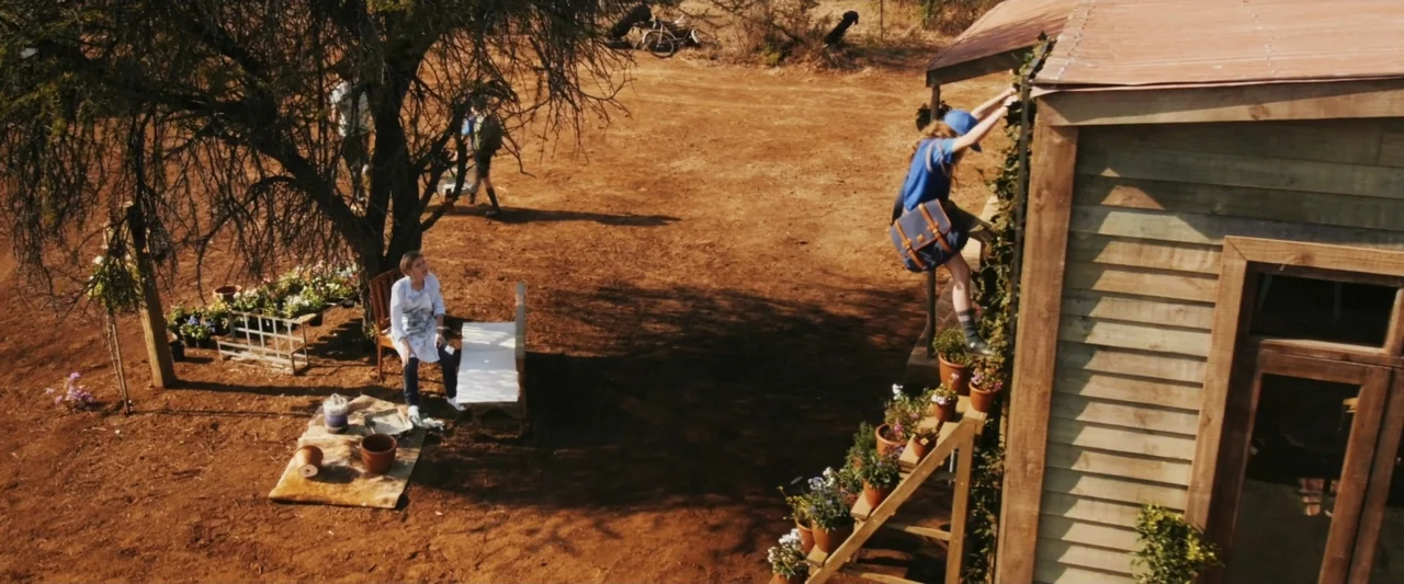Mia and the White Lion (2018) movie still: wide — A dry dirt backyard features a wooden shed and a large tree casting shadows. A child climbs the…