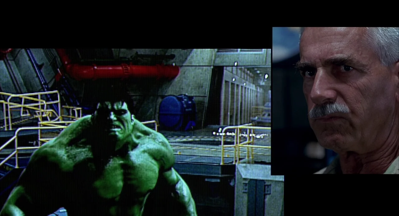 Hulk (2003) movie still: medium — A dark military command room contains a large television screen displaying a muscular creature. A man with a thick…