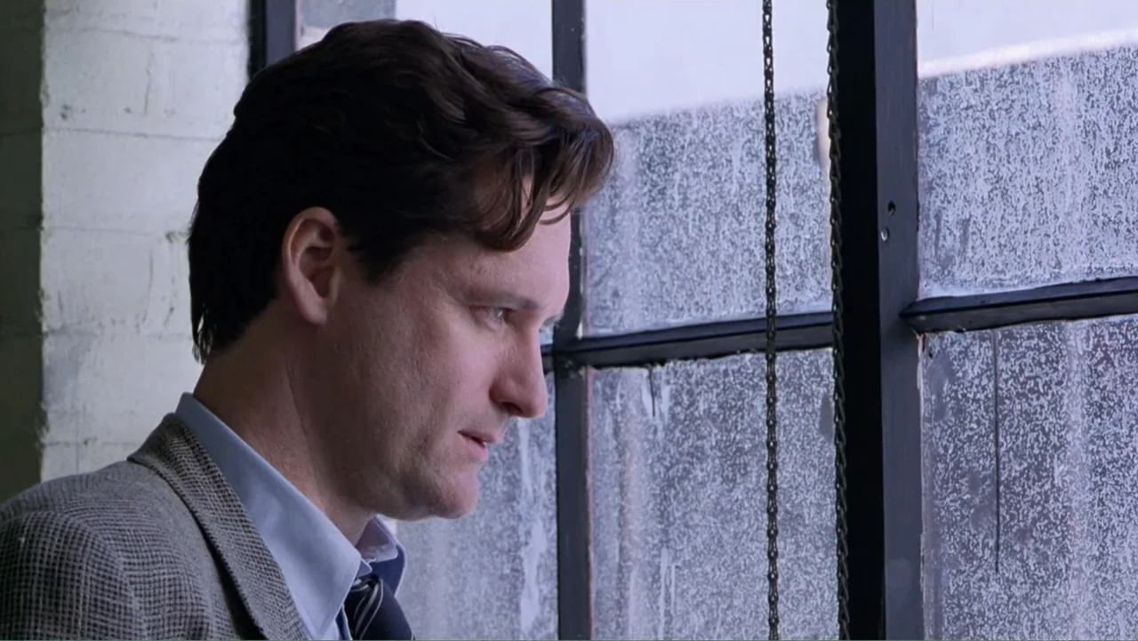 Mistrial (1996) movie still: closeup — A man stands near a large industrial window with a metal frame and frosted glass. He gazes outward through…