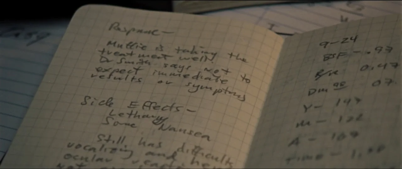 First Man (2018) movie still: closeup — An open notebook rests on a surface with handwritten notes on graph paper. The text details medical…