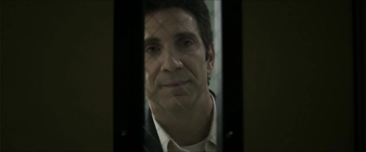 Heavenly Deposit (2019) movie still: closeup — A man stands behind a wire-reinforced glass pane in a sterile room. He looks directly through the…