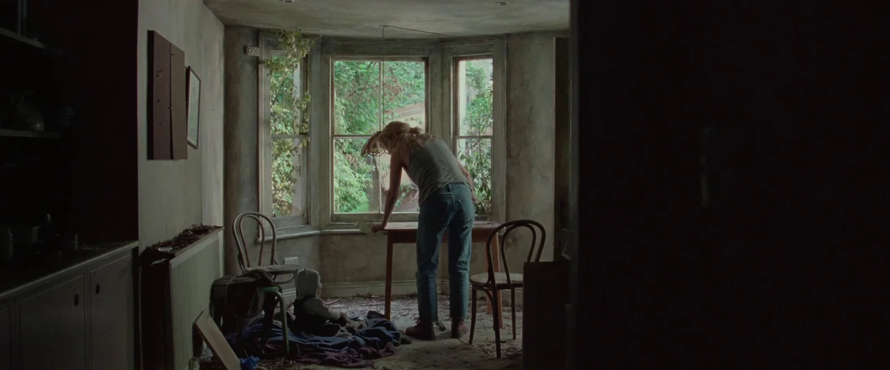 The End We Start From (2023) movie still: fullbody — A neglected room with peeling walls and debris on the floor features a bay window. A woman…