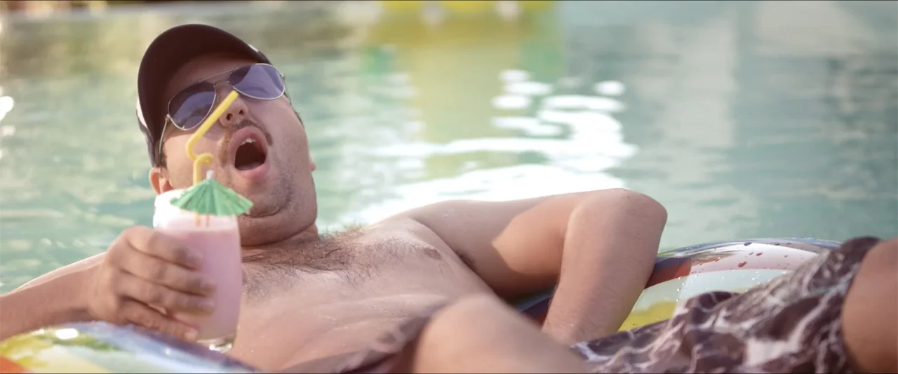 High Five (2004) movie still: medium — A man floats on a colorful inflatable ring in a bright blue pool. The man wears sunglasses and a baseball cap…