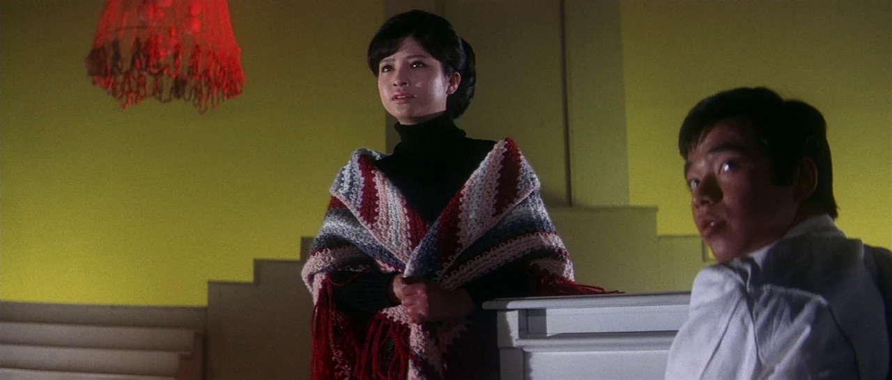 Tokyo Drifter (1966) movie still: medium — A dimly lit indoor staircase landing features yellow walls and a red hanging lamp. A woman wearing a…