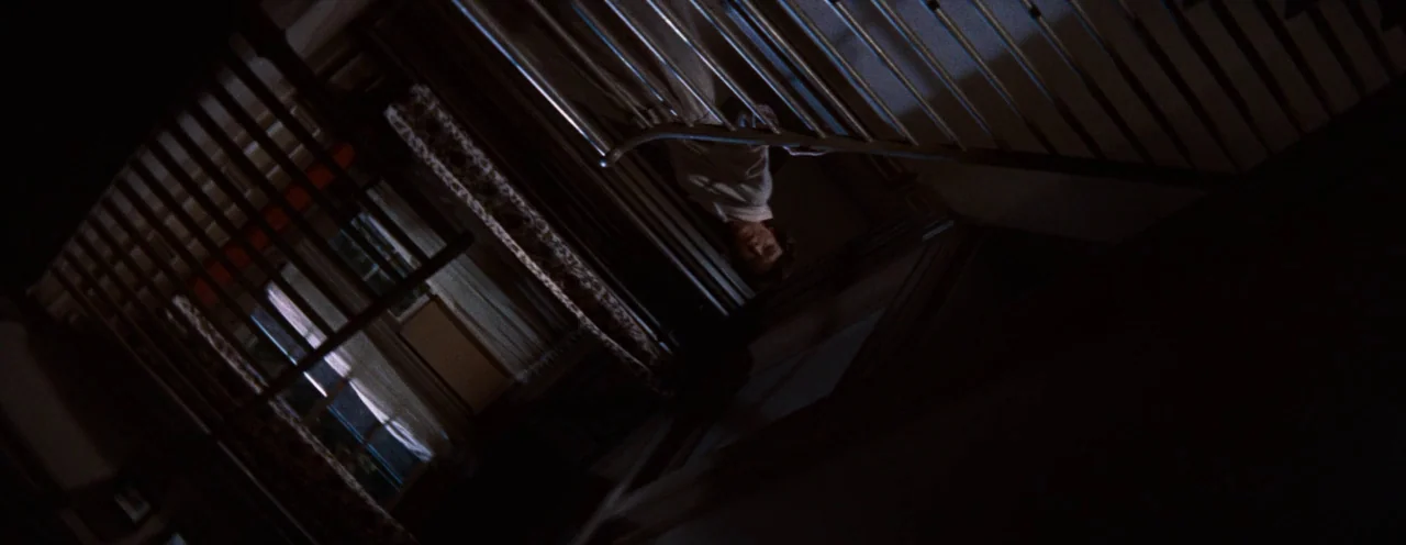 Rebel Without A Cause (1955) movie still: medium — An interior staircase is captured from a steep high angle in dim, dark conditions. A man in light…