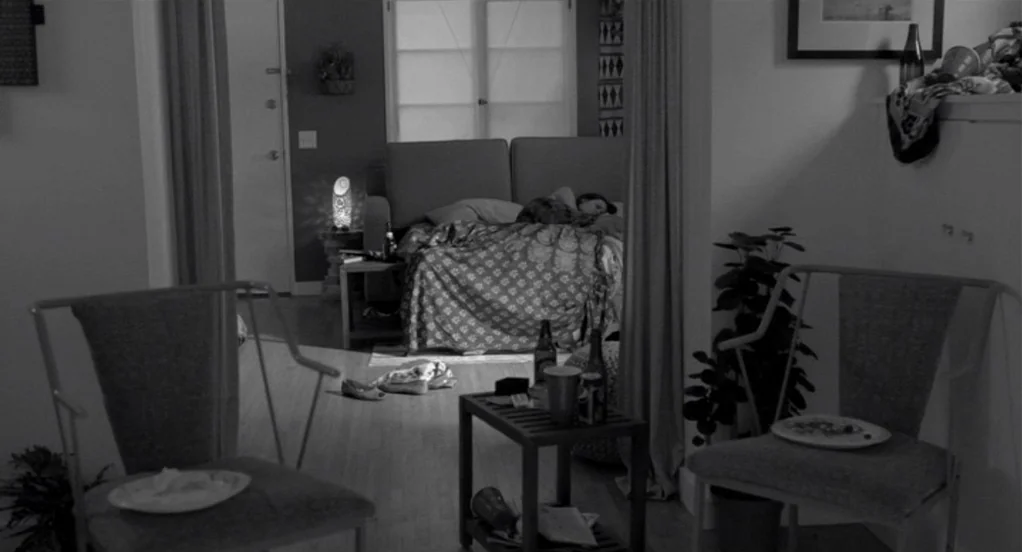 Much Ado About Nothing (2012) movie still: wide — A cluttered apartment interior with two chairs facing a central opening. A bed is visible in the…