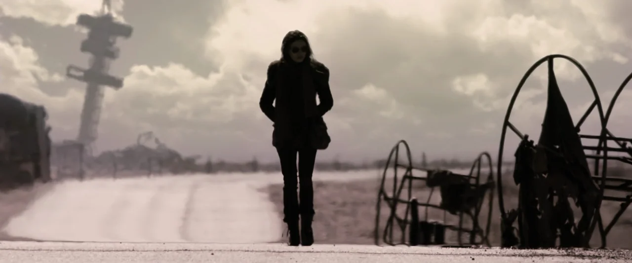 The Book of Eli (2010) movie still: fullbody — A flat, desolate landscape under a cloudy, overcast sky features scattered metallic debris. A young…