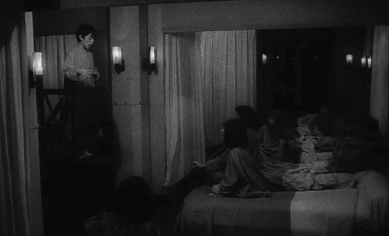 The Wild Child (1970) movie still: wide — A dimly lit dormitory with rows of beds and wall-mounted lamps. A young boy stands on an elevated…