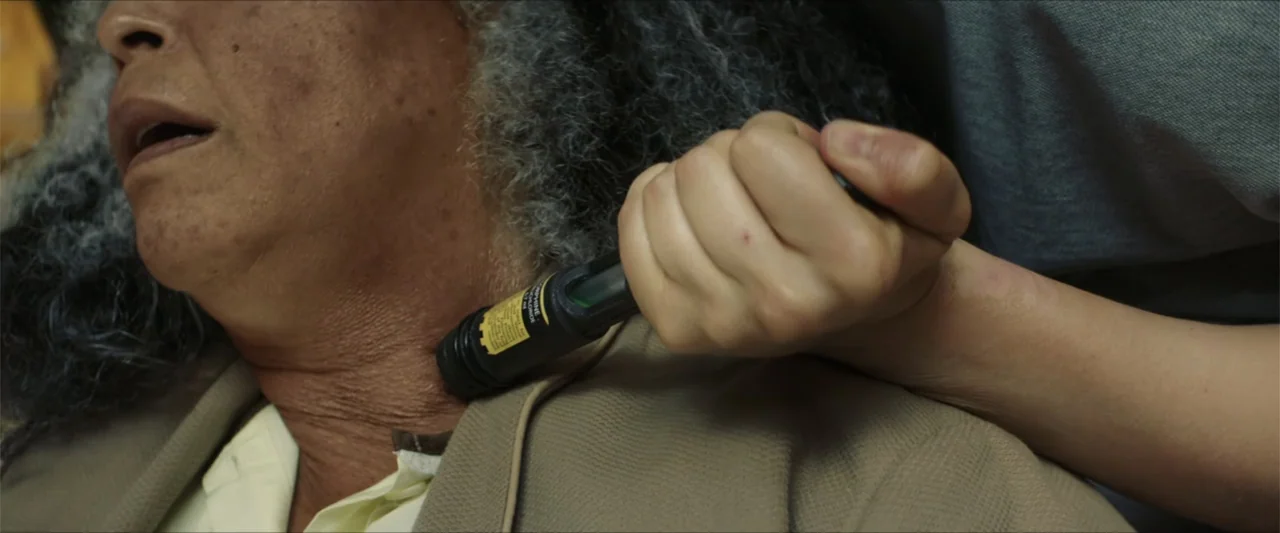 American Carnage (2022) movie still: closeup — An interior bedroom setting focuses on a close-up of a person being treated. A hand holds a medical…