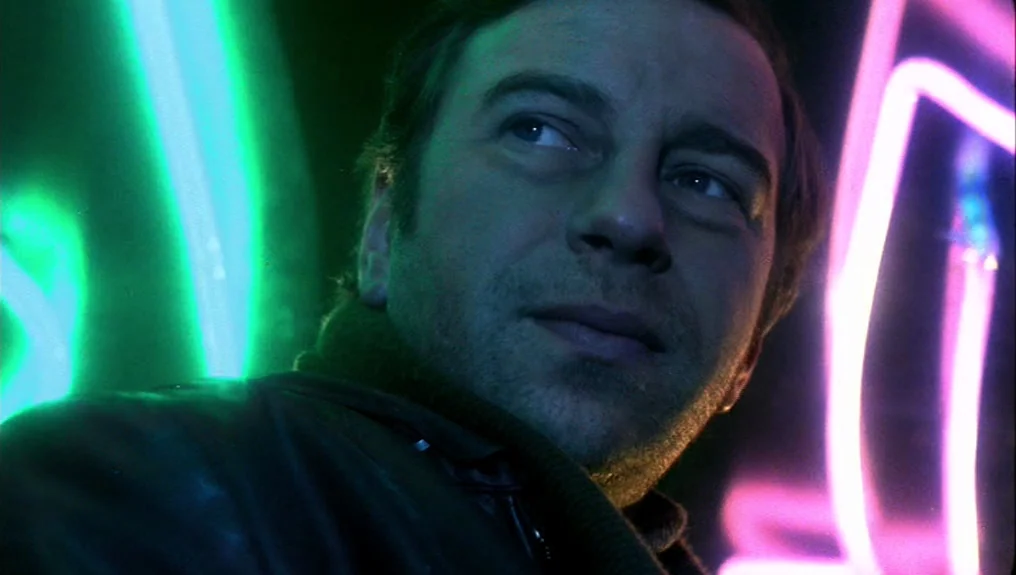 O-Bi, O-Ba: The End of Civilization (1985) movie still: closeup — A man stands in the dark illuminated by vibrant neon signs at night. He is…