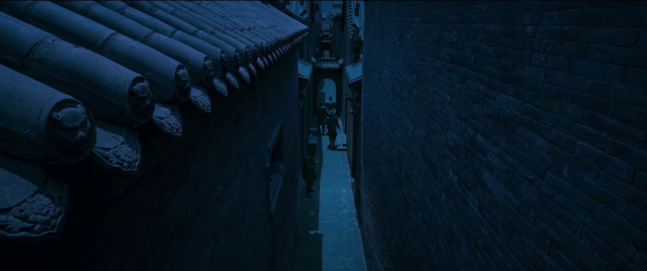 Full River Red (2023) movie still: wide — A narrow stone alleyway is flanked by tall brick walls and tiled roof structures. Three figures in dark…