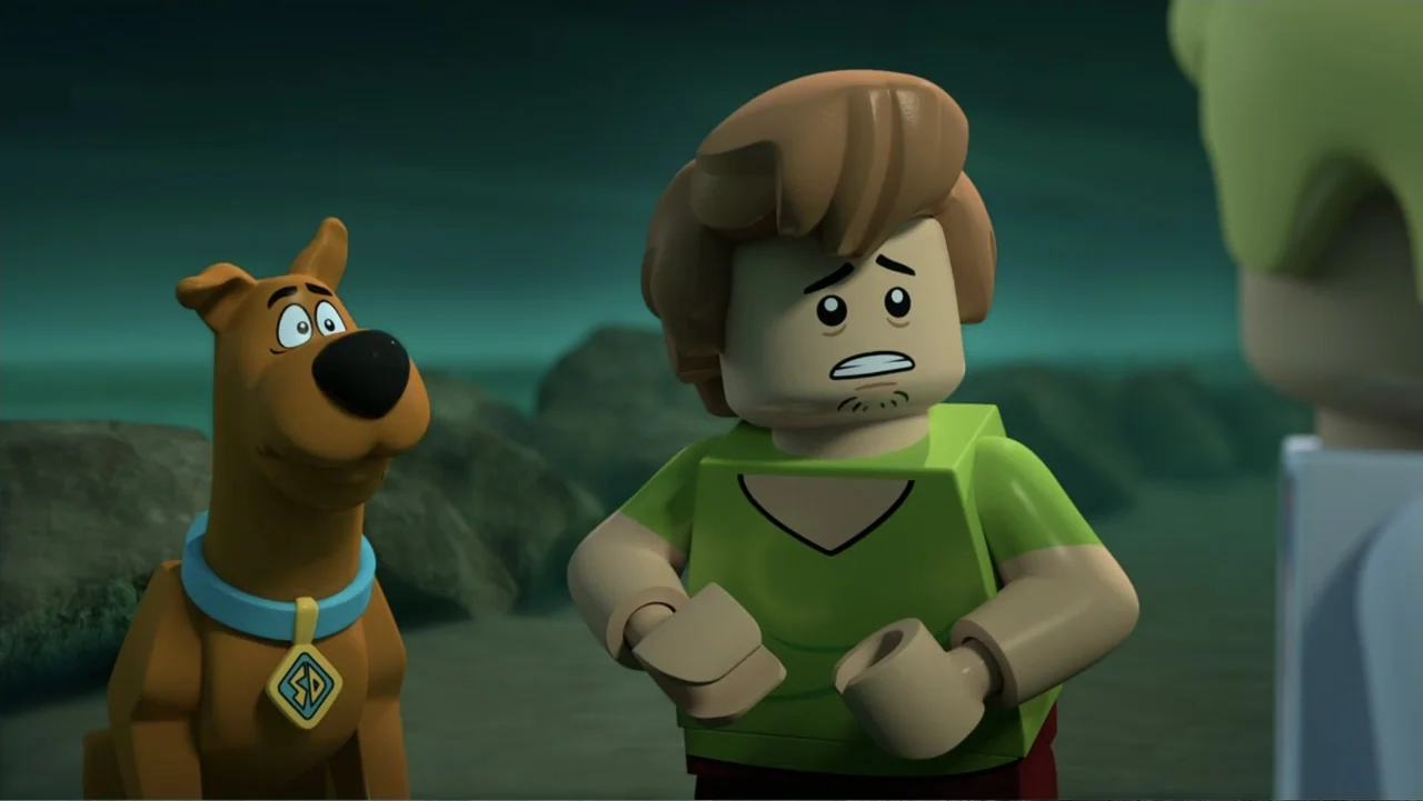 LEGO Scooby-Doo! Haunted Hollywood (2016) movie still: medium — A dark, misty beach at night with rocky terrain in the background. A brown dog and a…
