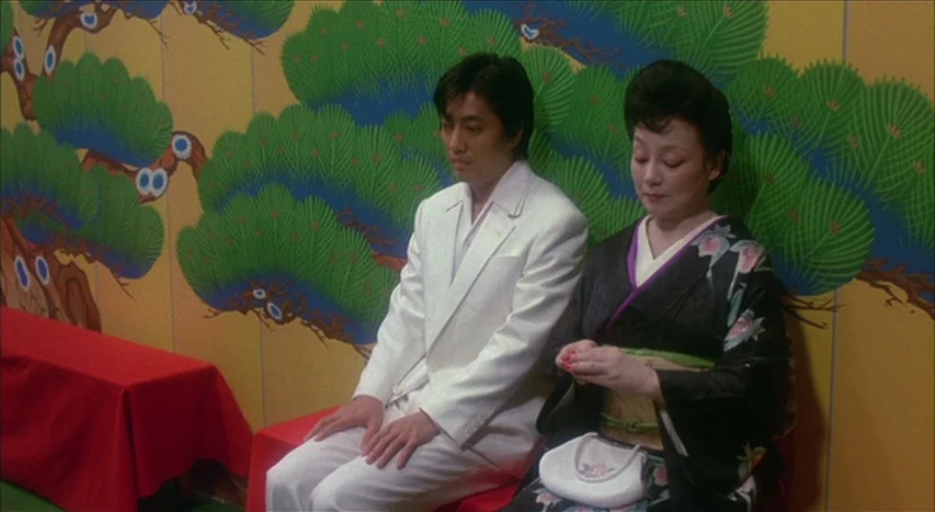 Mishima: A Life in Four Chapters (1985) movie still: medium — A room features a large yellow wall decorated with a bold, stylized pine tree mural.…