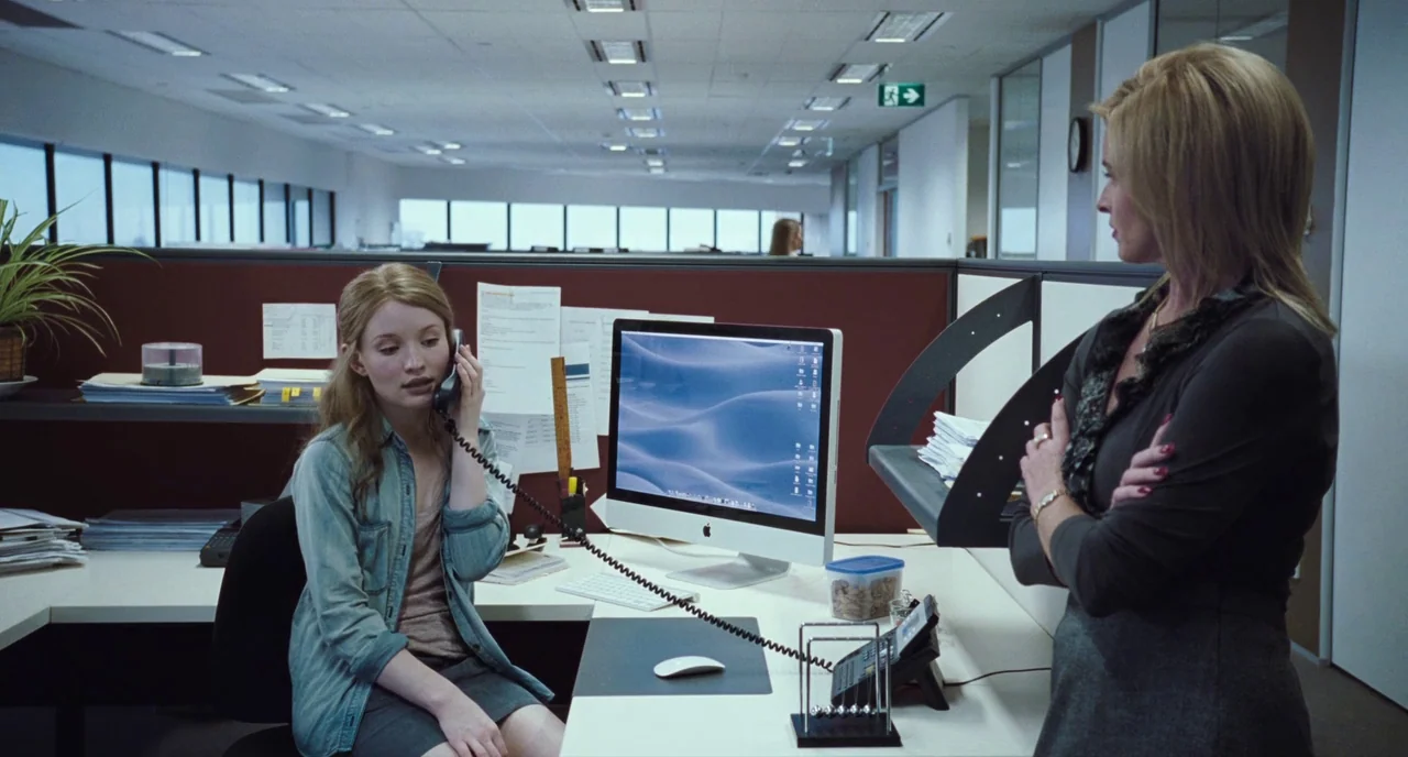 Sleeping Beauty (2011) movie still: medium — A modern corporate workspace features gray cubicle walls and white desks with computers. A younger…