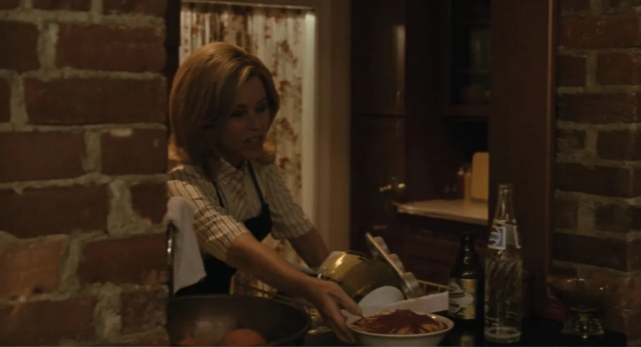 Call Jane (2022) movie still: medium — A domestic kitchen features a brick wall in the foreground and dish racks behind. A woman in a striped shirt…