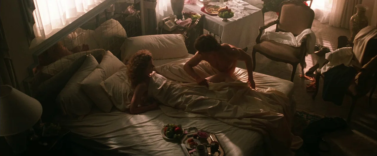 Days of Thunder (1990) movie still: wide — A hotel suite features a large bed, a table with fruit, and wooden furniture. A man and a woman interact…