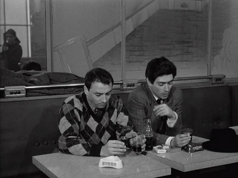 Band of Outsiders (Bande à part) (1964) movie still: medium — A cafe booth interior with dark upholstered seating and a mirrored wall behind it. Two…