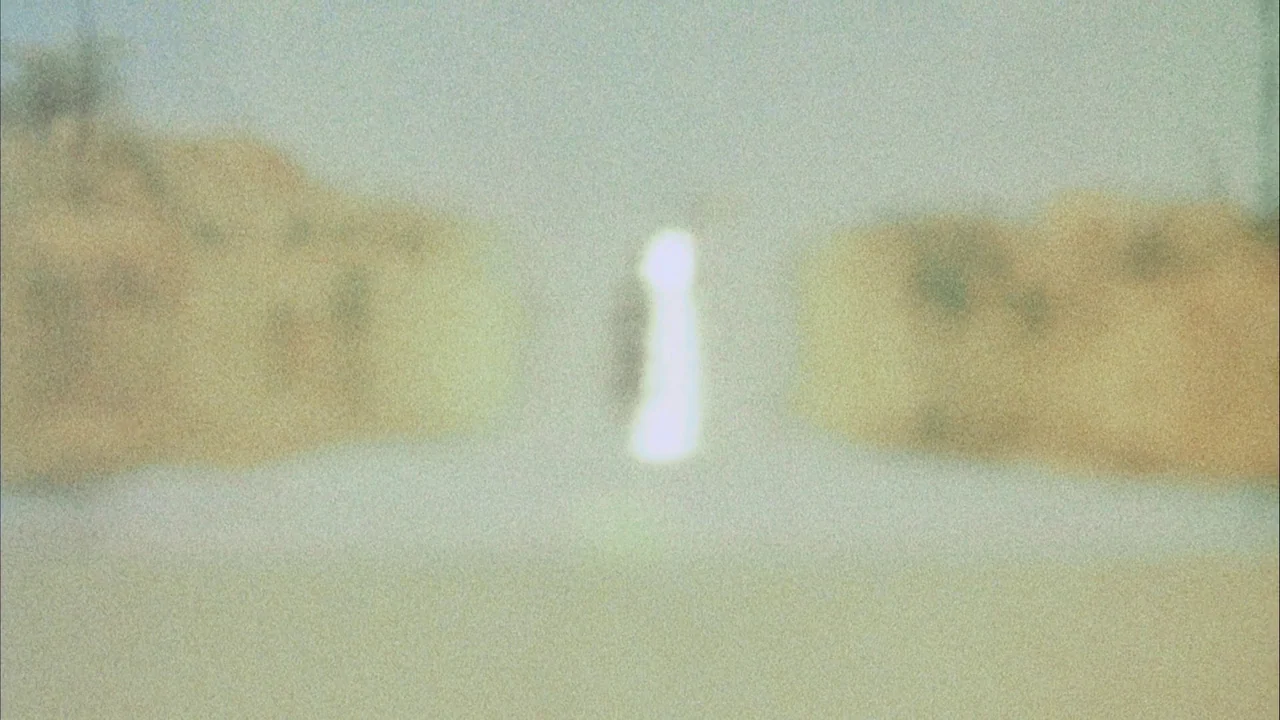 Phase IV (1974) movie still: wide — A vast, out-of-focus desert landscape with mounds rising on either side of the frame. A bright, intense flare of…
