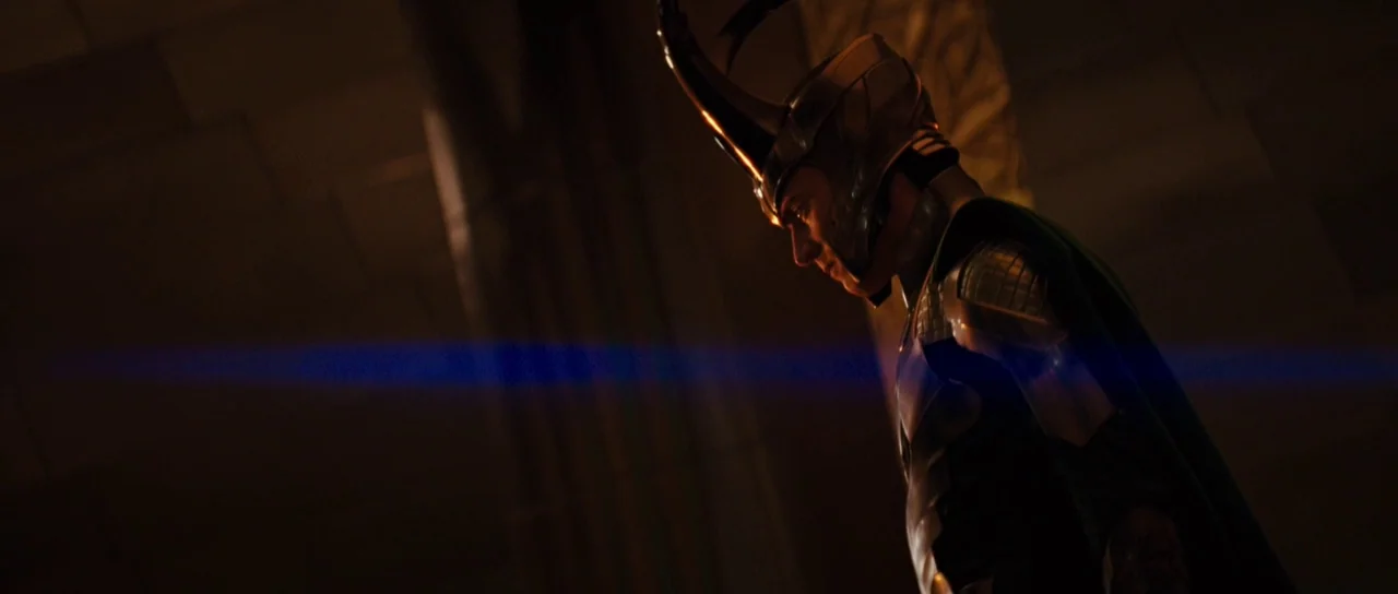 Thor (2011) movie still: medium — A dimly lit stone passage with geometric patterns carved into the wall surfaces. A figure in ornate armor and a…