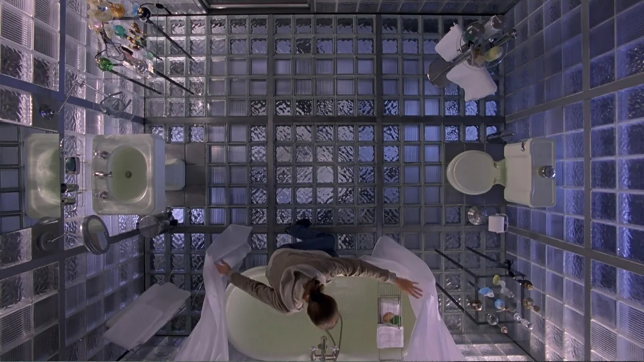 13 Ghosts (1960) movie still: wide — A modern bathroom features walls and a floor constructed from translucent glass blocks. A woman stands inside a…