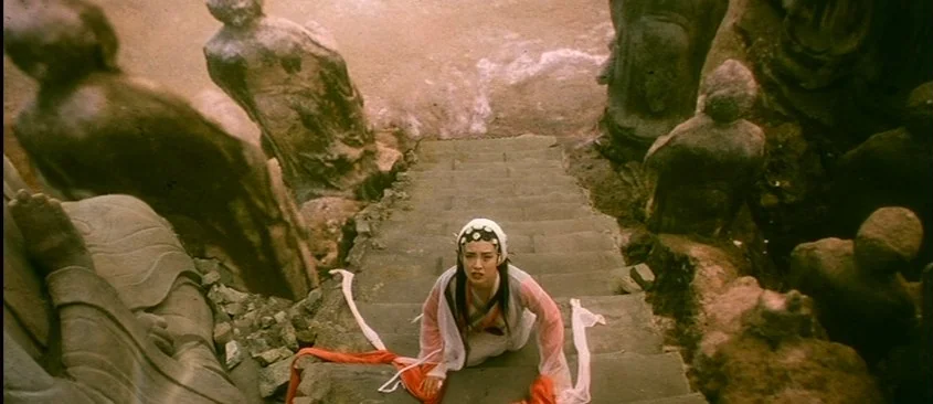 Green Snake (1993) movie still: wide — A woman crawls up a stone staircase flanked by multiple weathered stone statues. The environment is textured…