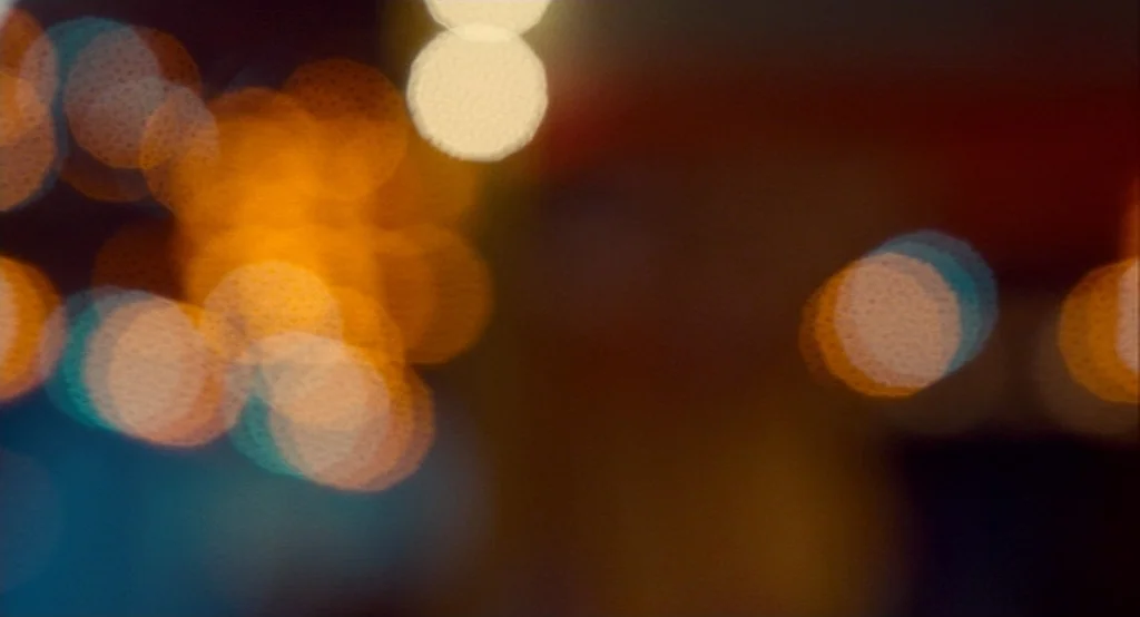 Adventureland (2009) movie still: establishing — A night scene reduced to abstract circles of light from out-of-focus street lamps. These luminous…