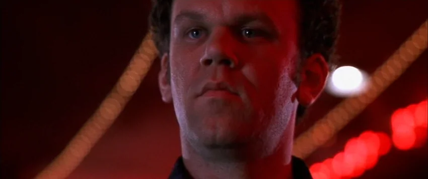 Hard Eight (1996) movie still: closeup — A dimly lit interior space filled with red neon lighting. A man looks forward against a dark, blurred…
