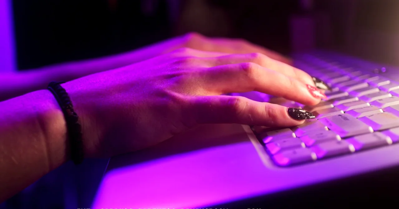 T Blockers (2023) movie still: closeup — A close view shows a hand with glittery nails resting on a white laptop keyboard. The area is illuminated…