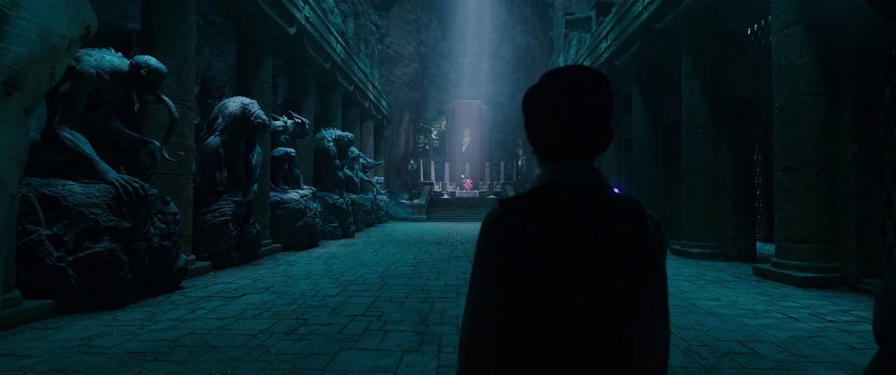 Shazam! (2019) movie still: wide — A vast stone hall lined with gargoyle statues leads toward a distant raised dais. A silhouette of a young boy…