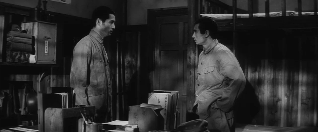The Human Condition II: Road to Eternity (1959) movie still: medium — A dimly lit room with wooden walls, metal cabinets, and a bunk bed. Two men in…