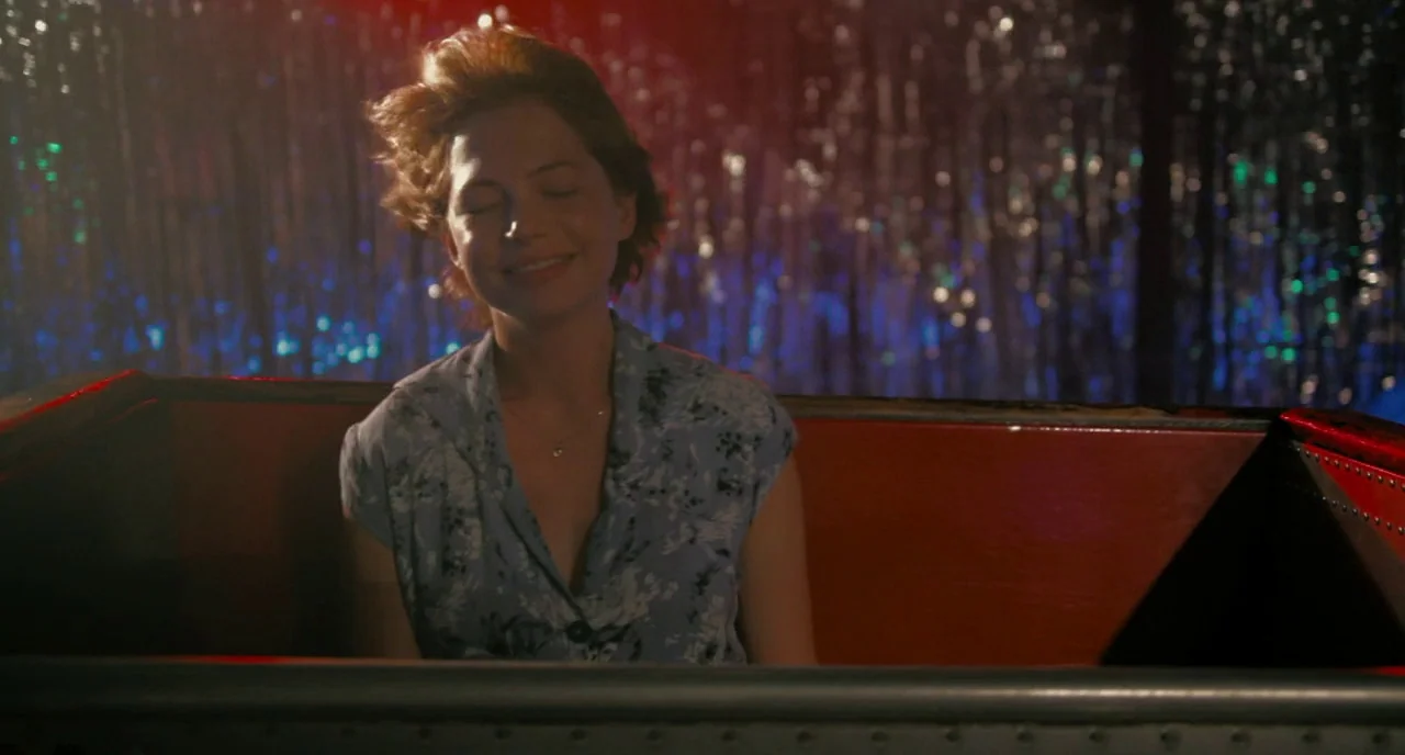 Take This Waltz (2011) movie still: medium — A woman sits inside an amusement park ride car lined with red padding. Metallic foil streamers reflect…