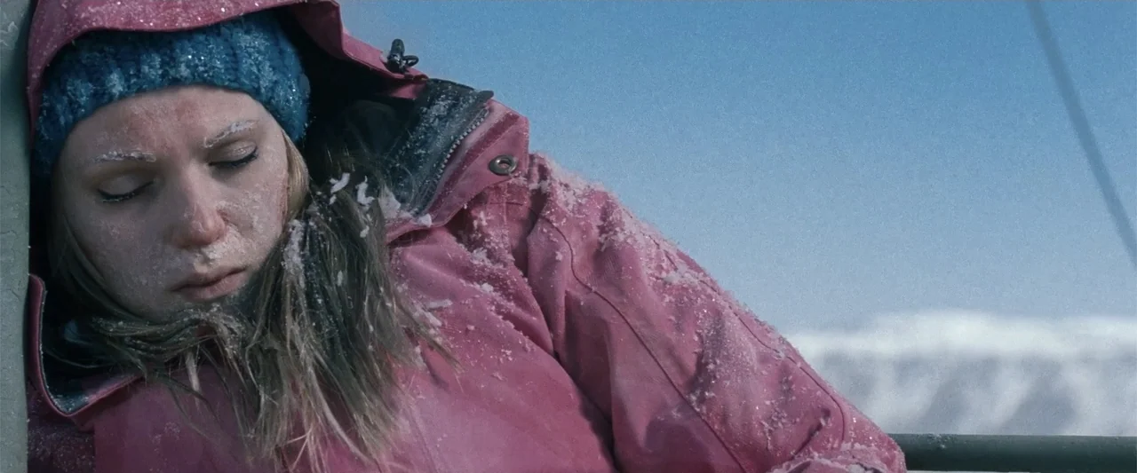 Frozen (2010) movie still: medium — A woman sits outdoors on a ski lift surrounded by snowy mountain peaks. She wears a pink jacket and blue beanie…
