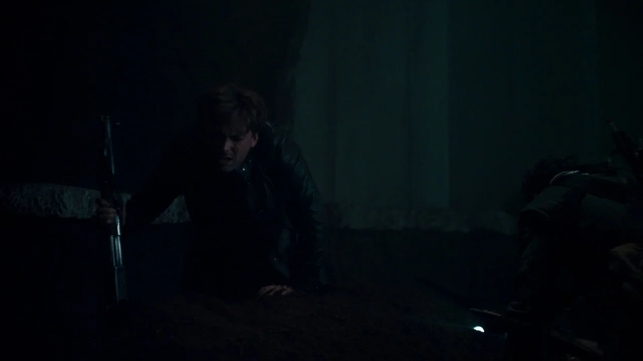 Fright Night (2011) movie still: medium — A dark, cramped underground space with rough stone or concrete surfaces. A man grips a rifle while leaning…