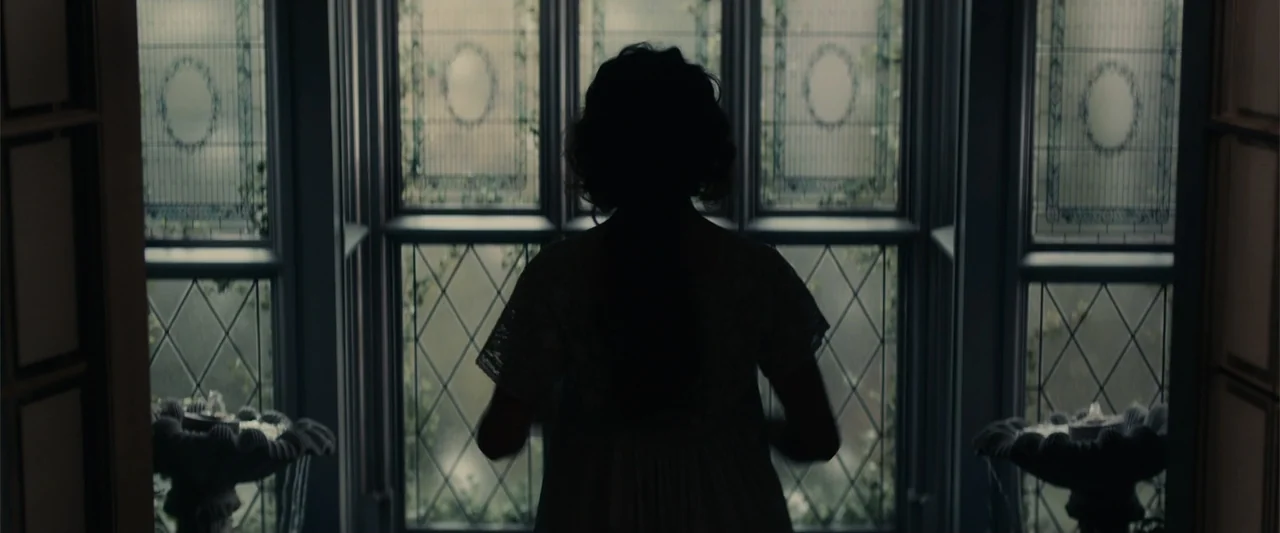 Winter's Tale (2014) movie still: medium — A window alcove with ornate leaded glass panes looking out onto overcast daylight. A person stands facing…