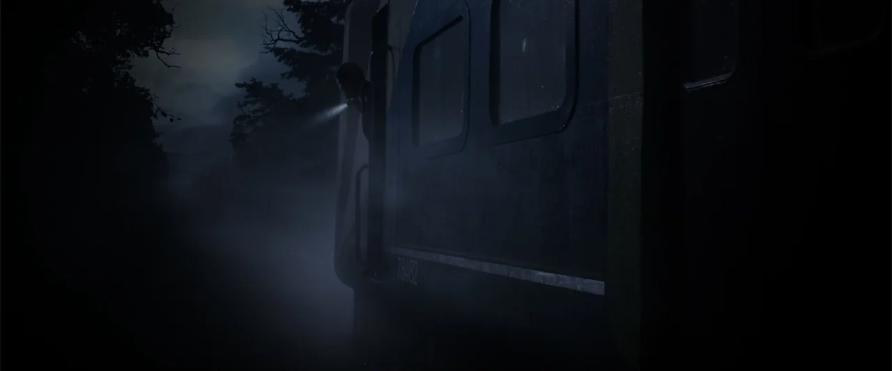 Howl (2015) movie still: wide — A dark, foggy outdoor setting beside a stationary train at night. A person reaches from the train doorway to shine a…