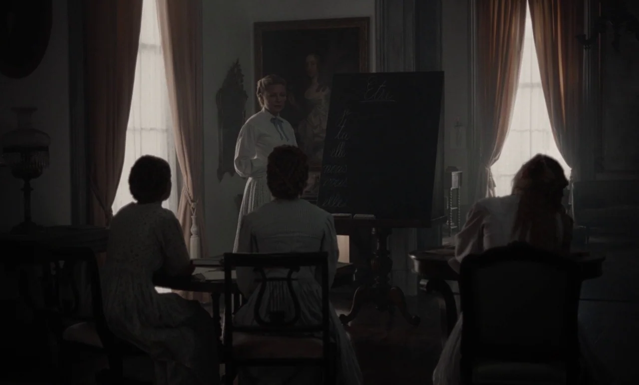 The Beguiled (2017) (2017) movie still: wide — A dimly lit 19th-century schoolroom features tall windows draped with heavy fabric curtains. A…