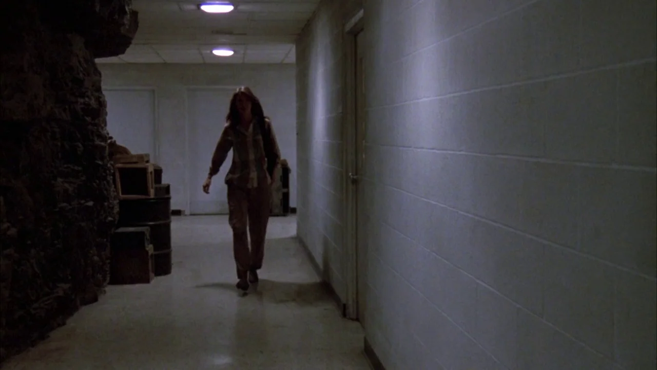 Day of the Dead (1985) movie still: fullbody — A long, dimly lit basement corridor has white cinder block walls and a tile floor. A woman walks…