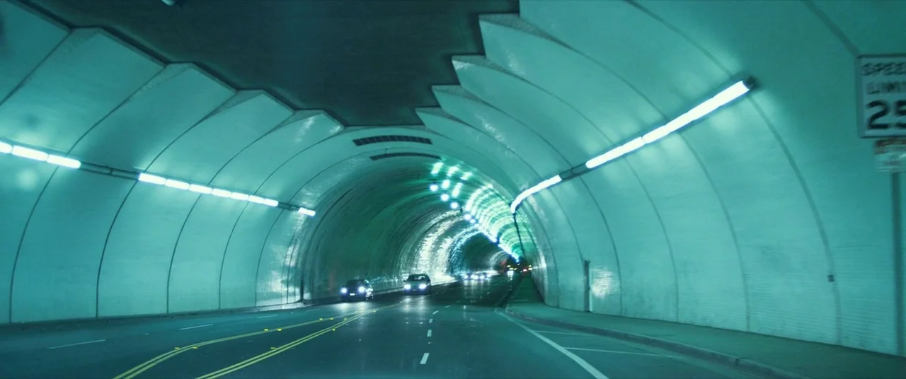 Maniac (2012) movie still: establishing — A curved road tunnel features smooth arched walls illuminated by continuous fluorescent lighting strips.…
