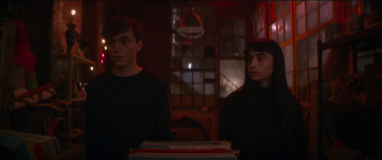 Humanist Vampire Seeking Consenting Suicidal Person (2023) movie still: medium — A dark space filled with vinyl record bins and dim red lighting. A…