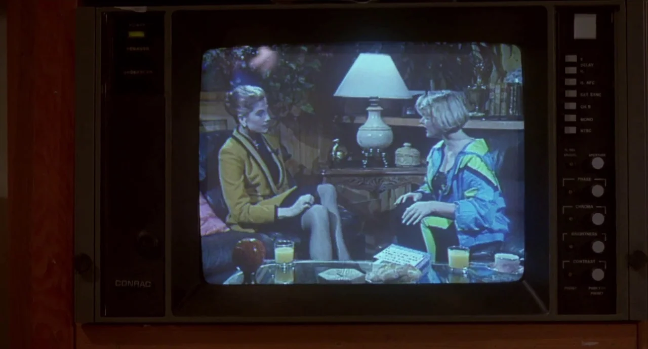 Hellraiser III: Hell on Earth movie still: medium — Two women sit on a leather couch inside a warmly lit room shown on a monitor. A glass table…
