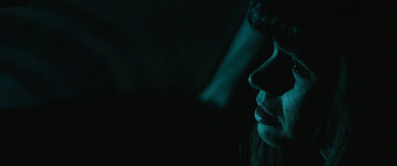 Southbound (2015) movie still: closeup — A dark car interior at night with minimal ambient light. A woman's profile is lit by a faint blue light…