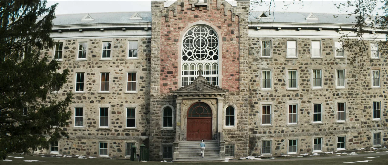 The Sacrifice Game (2023) movie still: wide — A large multi-story stone building features a central rose window and symmetrical arched doorway. A…