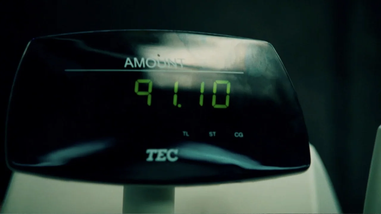 Hancock (2008) movie still: closeup — A close-up view of a digital checkout scale display shows green numeric digits. The unit is black with the…